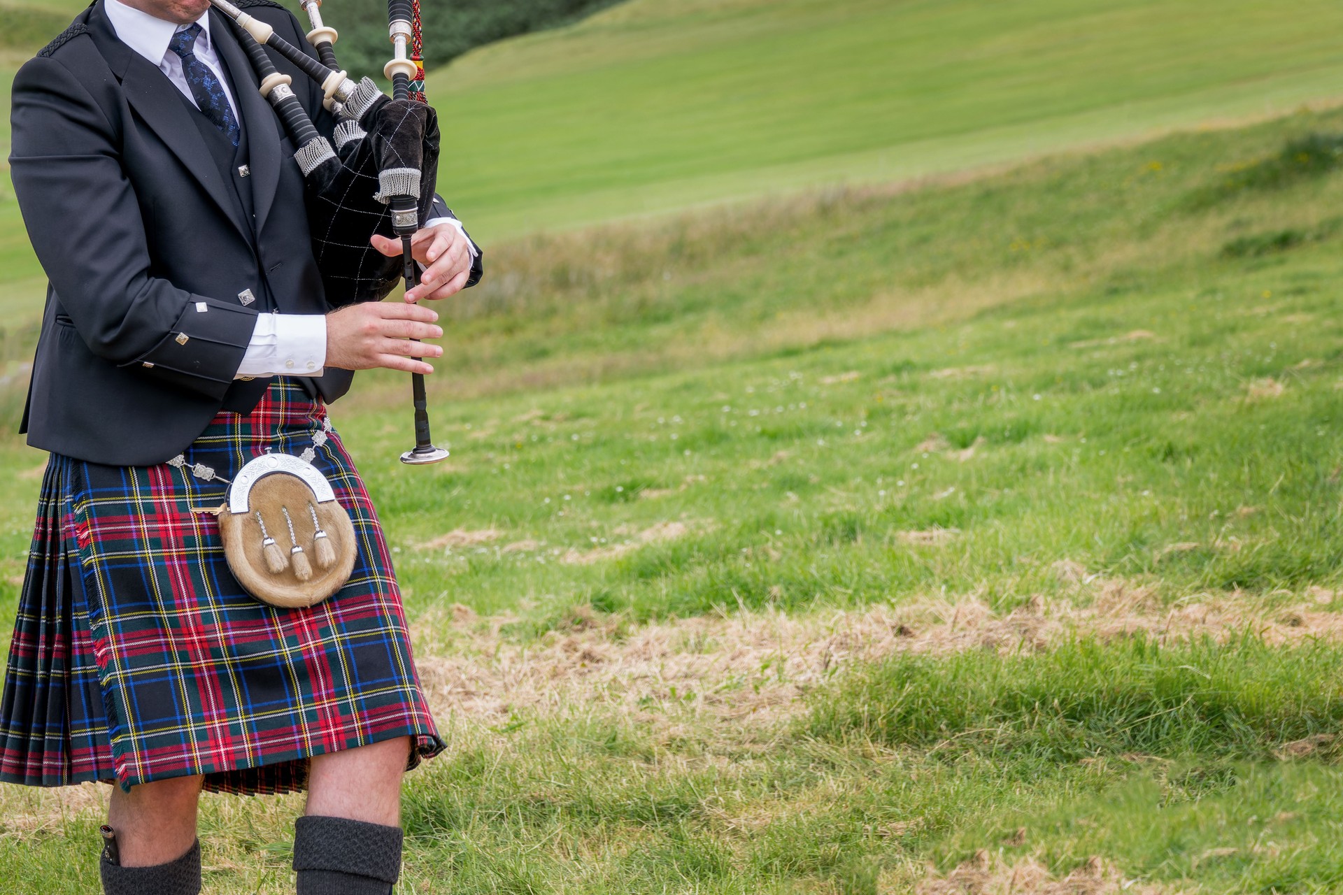 Bagpiper in traditional Highland dress playing the Great Highland Bagpipe outdoors